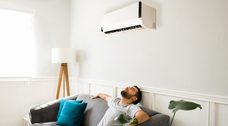 homme sur son canapé en dessous d'une climatisation 