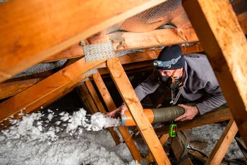 Artisan qui projette de l'isolant par soufflage sur combles perdus